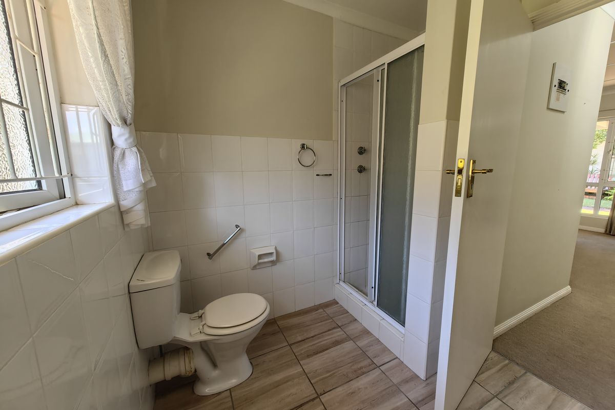 A functional bathroom featuring a shower enclosure, toilet, and neutral wall tiling with wood-look floor tiles.