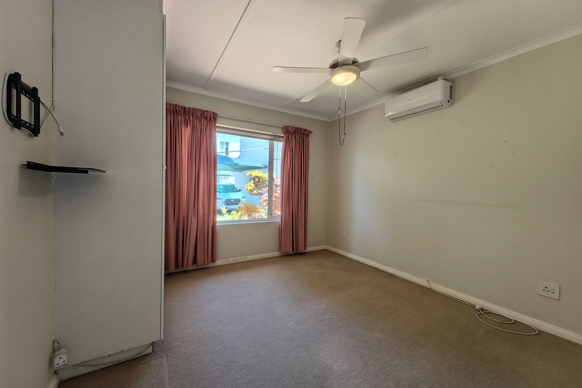 A vacant bedroom featuring neutral carpet, a ceiling fan, and a wall-mounted air conditioning unit, offering a blank canvas for personalization.