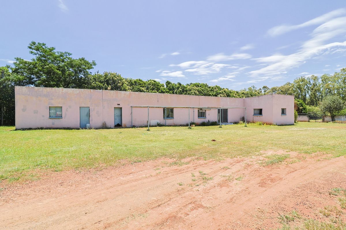 Rear view of a single-story small holding dwelling featuring a large open lawn, metal pergola structure, and weathered exterior wall finishes.