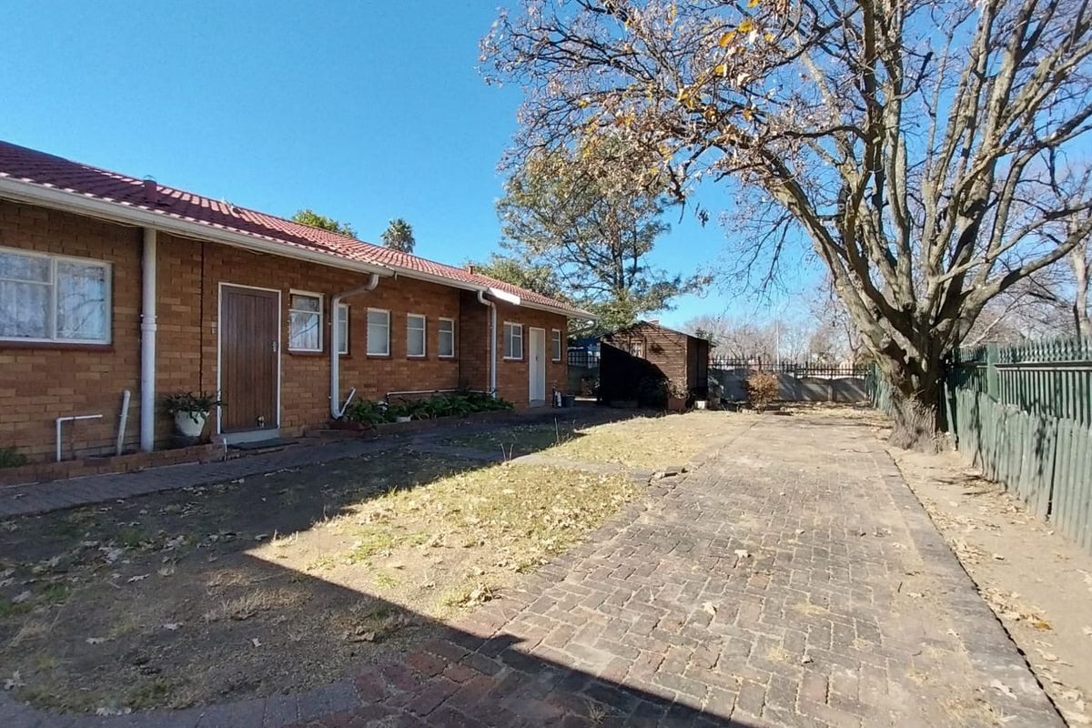 A view of the rear exterior of a brick house featuring a paved driveway, a small garden area, and a detached storage shed.
