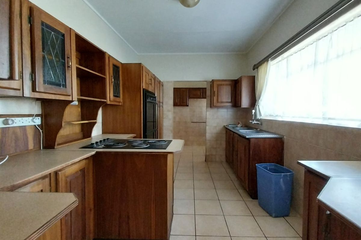 A functional kitchen featuring traditional wooden cabinetry, built-in oven, hob, and tiled flooring with ample natural light from a large window.