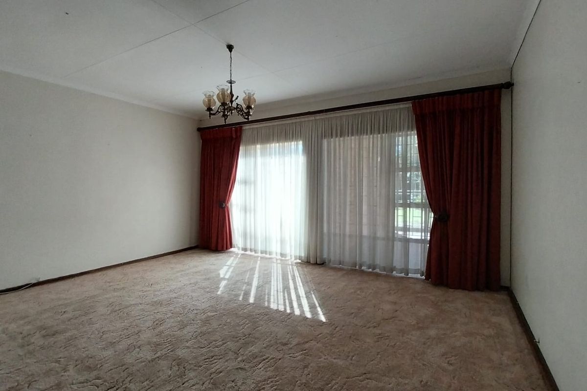 A spacious, empty living room featuring neutral walls, carpeted flooring, and large sliding glass doors with classic drapery.