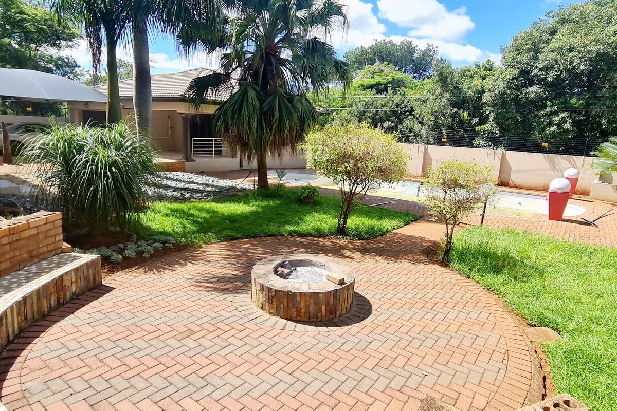 Spacious rear garden featuring a brick-paved patio area with a built-in fire pit, swimming pool, and established landscaping.