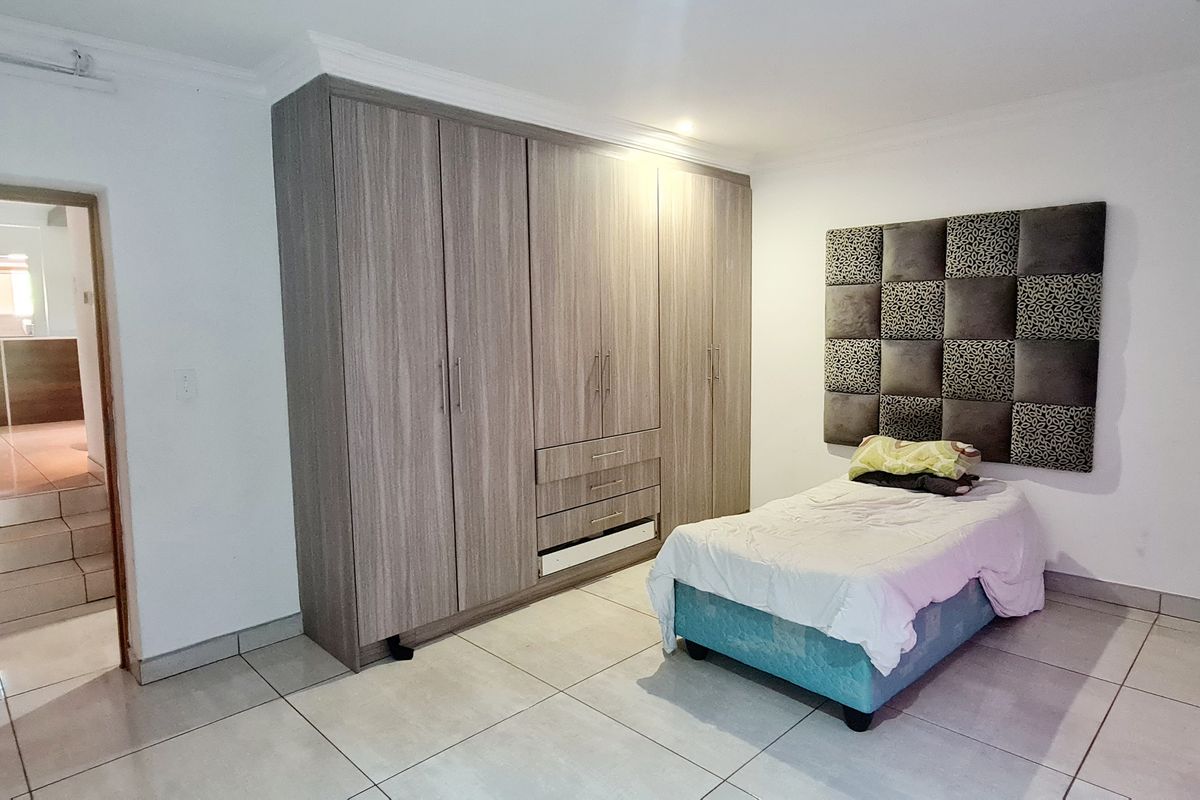 A bedroom featuring neutral tiled flooring, coving, and extensive built-in wooden cupboards providing ample storage space.