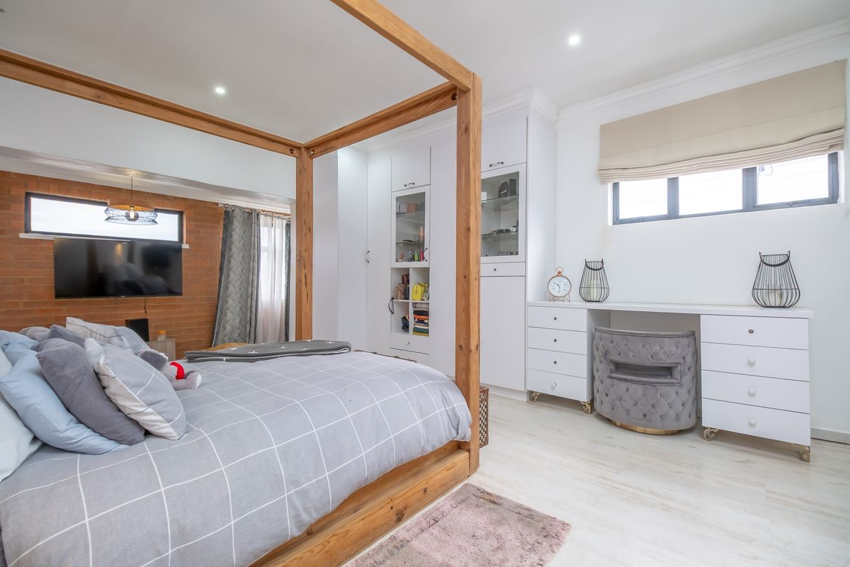 A well-appointed bedroom featuring built-in white cabinetry, a integrated vanity desk, recessed lighting, and a feature brick wall in the adjoining space.