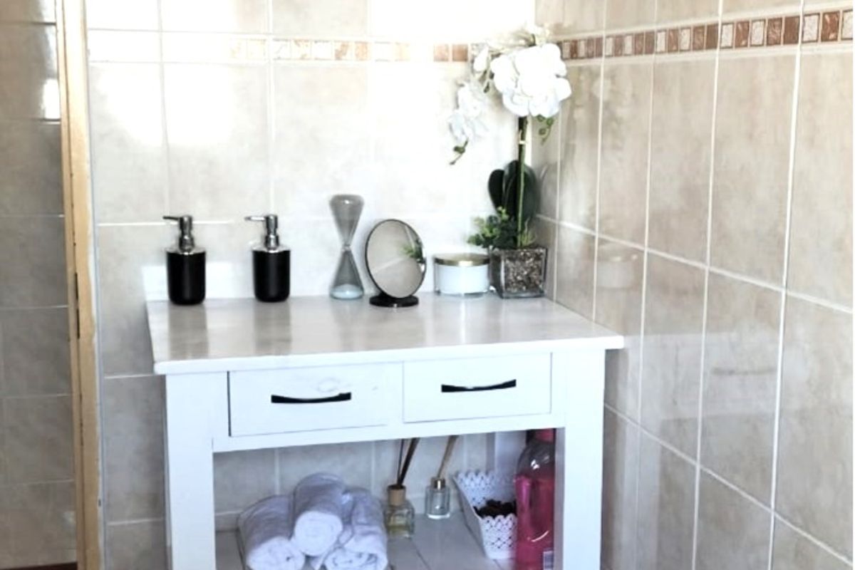 A bathroom featuring neutral ceramic wall and floor tiles with a white vanity unit.