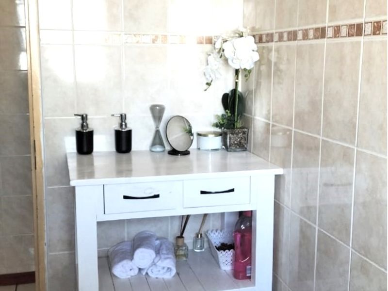 A bathroom featuring neutral ceramic wall and floor tiles with a white vanity unit.