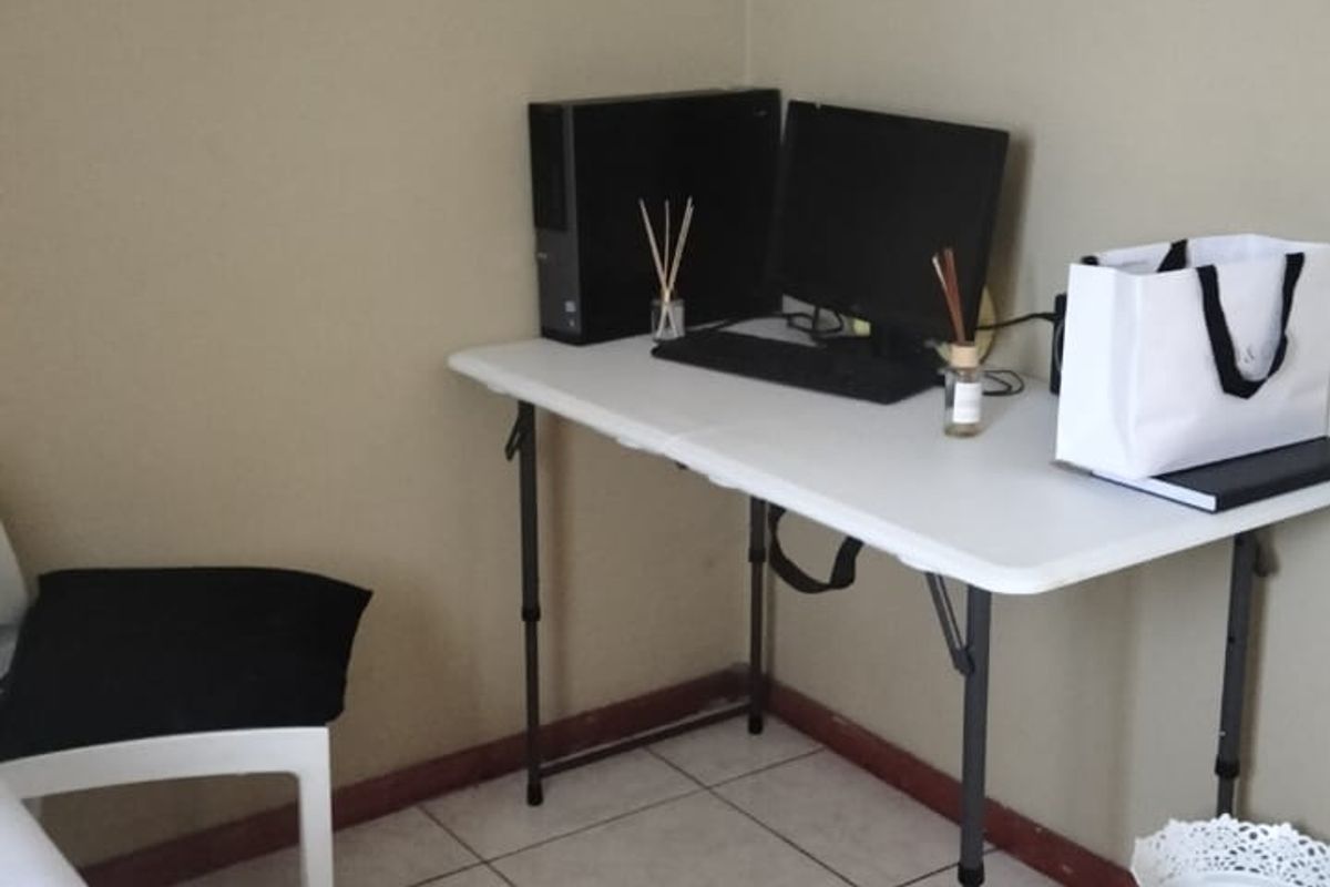 A bedroom corner featuring neutral wall paint and tiled flooring, currently utilized as a functional workspace area.