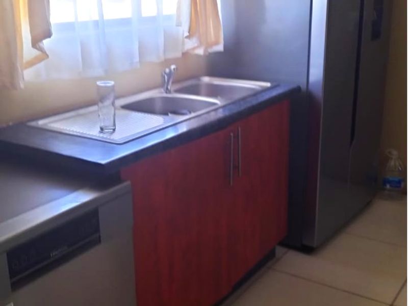 A functional kitchen area featuring a double sink, laminate countertops, and built-in cabinetry with tiled flooring.
