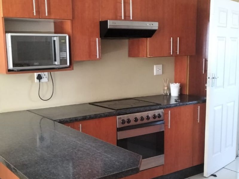 A functional kitchen featuring wood-finish cabinetry, granite countertops, a built-in oven with hob, and tiled flooring.