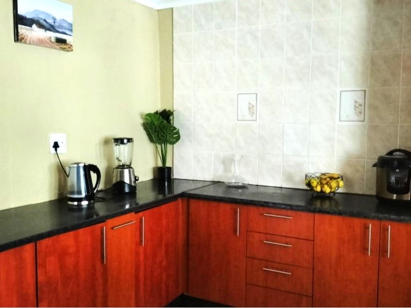 A functional kitchen featuring wood-look laminate cabinetry, dark laminate countertops, and neutral ceramic wall tiling.