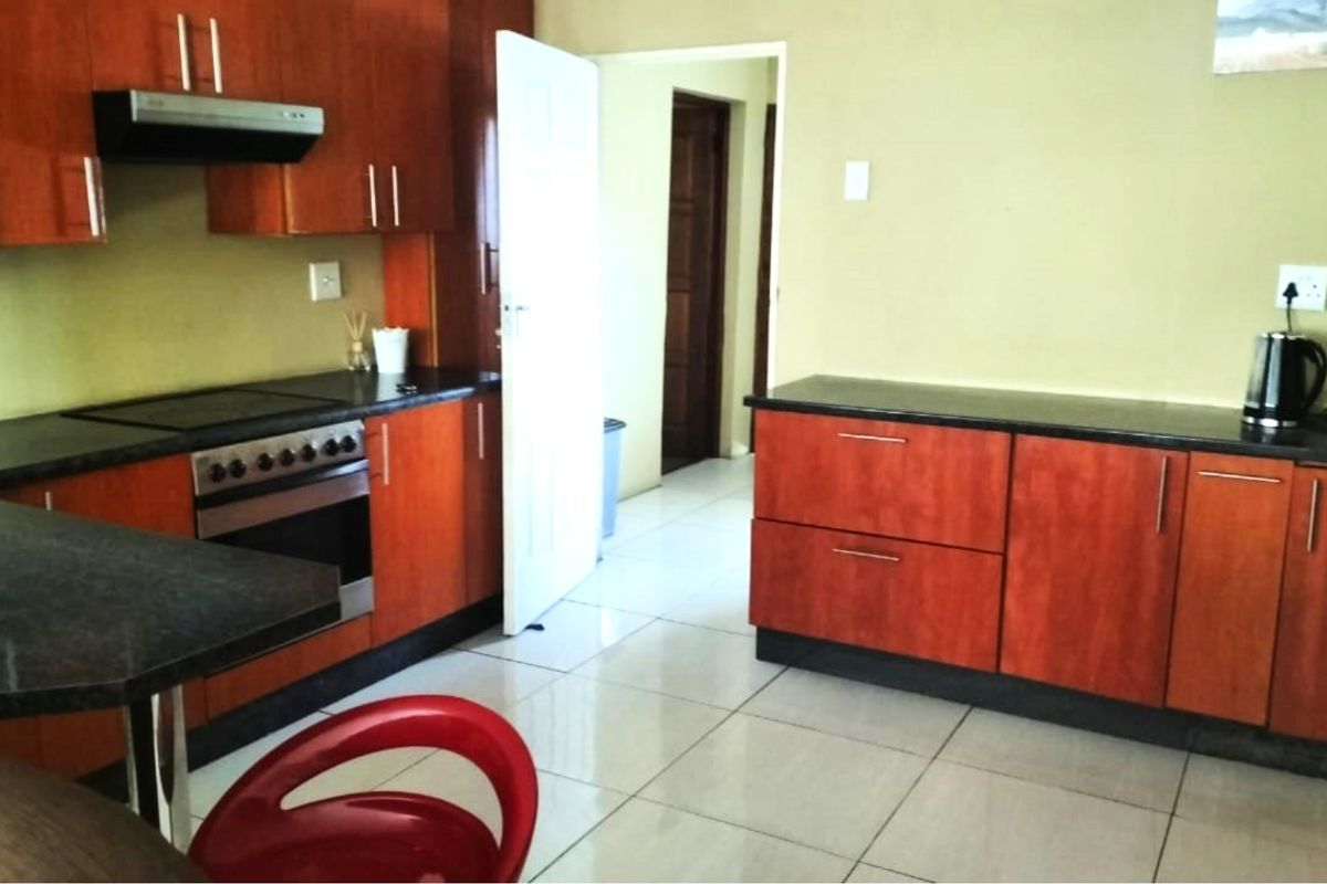 A functional kitchen featuring wood-finish cabinetry, dark granite countertops, built-in oven with extractor fan, and light-colored floor tiles.
