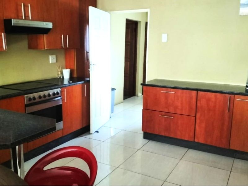 A functional kitchen featuring wood-finish cabinetry, dark granite countertops, built-in oven with extractor fan, and light-colored floor tiles.