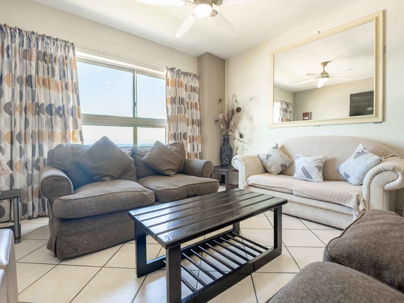 A comfortable living room featuring tiled flooring, a ceiling fan, and a large wall-mounted mirror, providing a bright and functional space.
