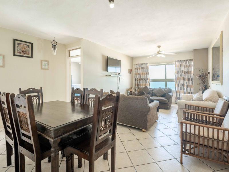 Open-plan living and dining area featuring tiled flooring, a ceiling fan, and large windows with natural light.