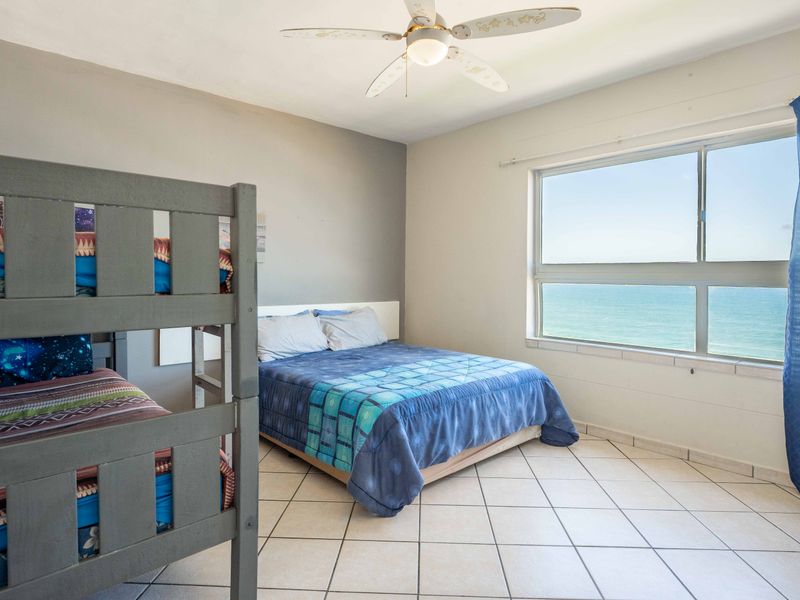 A spacious bedroom featuring tiled flooring, a ceiling fan, and a large window offering expansive ocean views.