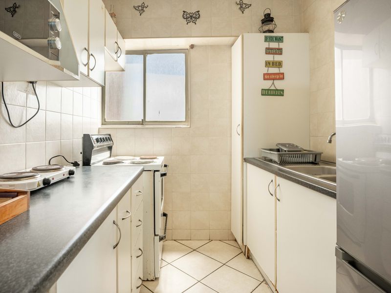 Compact kitchen featuring white cabinetry, laminate countertops, tiled backsplash, and a functional layout with a freestanding stove and stainless steel sink.