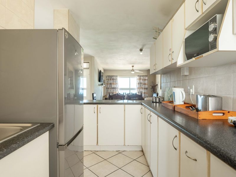 Open-plan kitchen featuring white cabinetry, dark laminate countertops, and tiled flooring, flowing into the adjacent living and dining area.