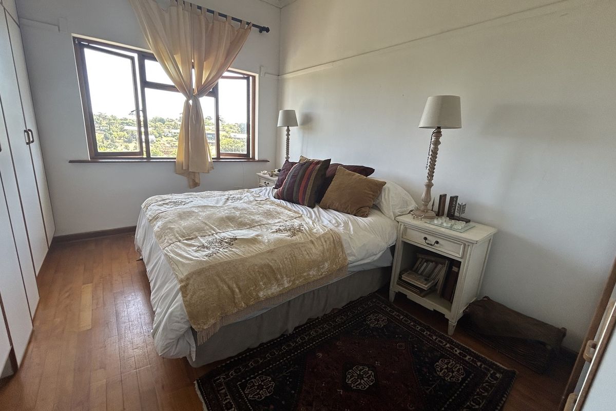 A well-lit bedroom featuring polished timber flooring, built-in wardrobe storage, and a large window providing natural light and elevated views.