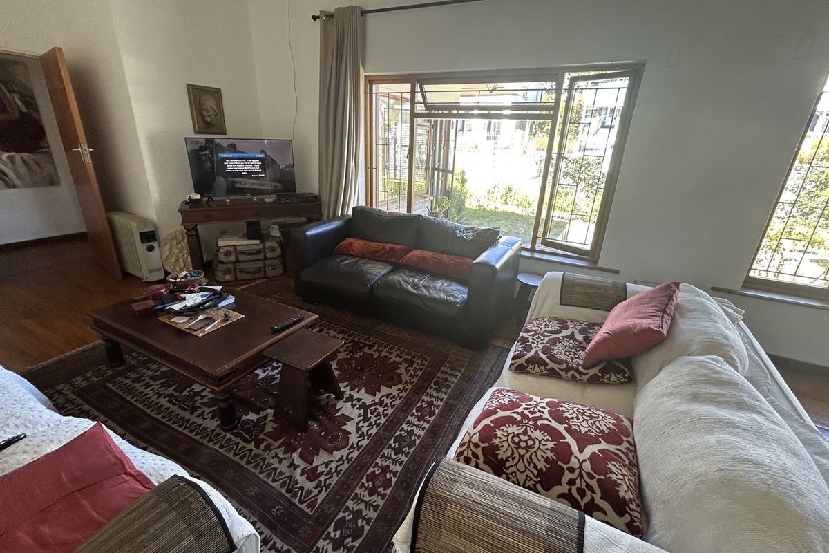 A comfortable living room featuring hardwood flooring and large windows with security bars, providing natural light and a view of the garden.