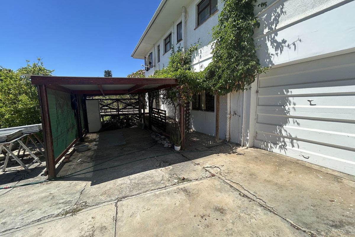 Rear exterior view showing a concrete driveway, attached carport structure, and garage access with visible weathering and surface cracking.