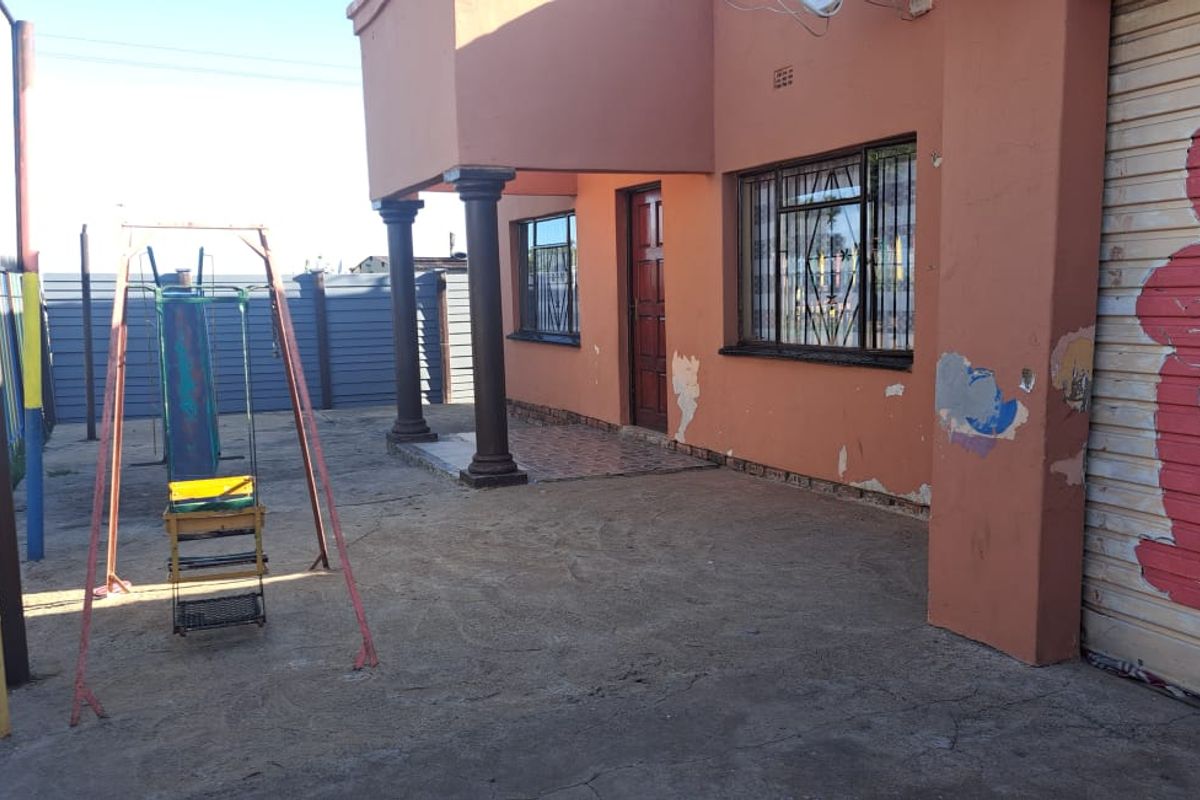 Exterior view of the property featuring a covered patio area, concrete paving, and security bars on windows.