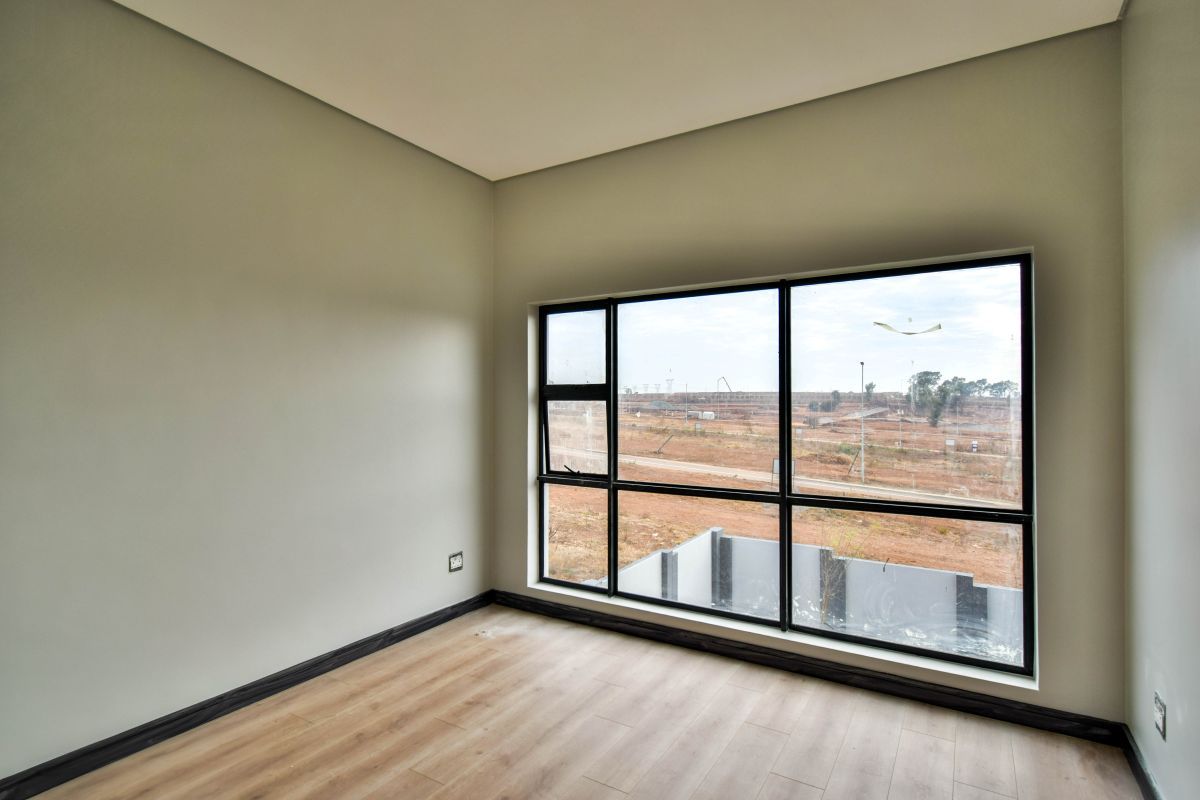 A bright, empty bedroom featuring modern wood-look flooring, neutral walls, and large black-framed windows offering an expansive view of the surrounding area.