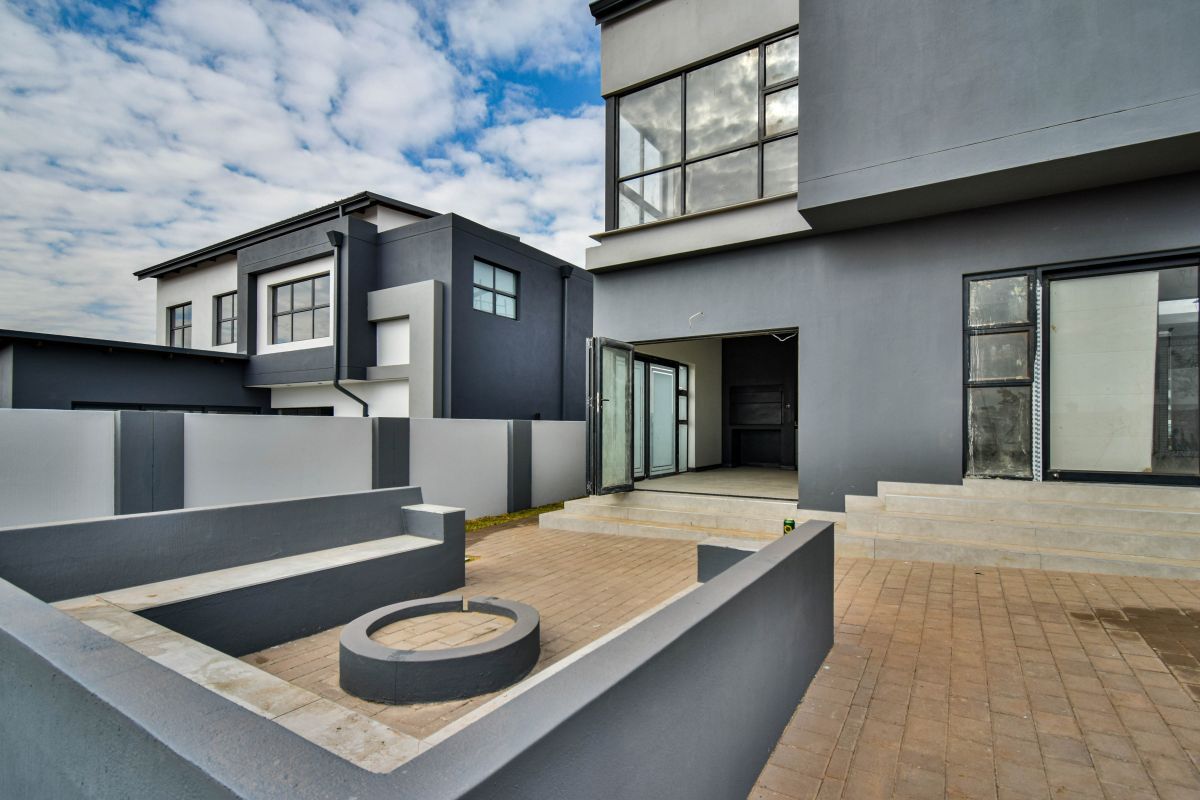 Modern rear exterior featuring a paved patio area with a built-in fire pit, concrete seating, and direct access to the home through glass doors.