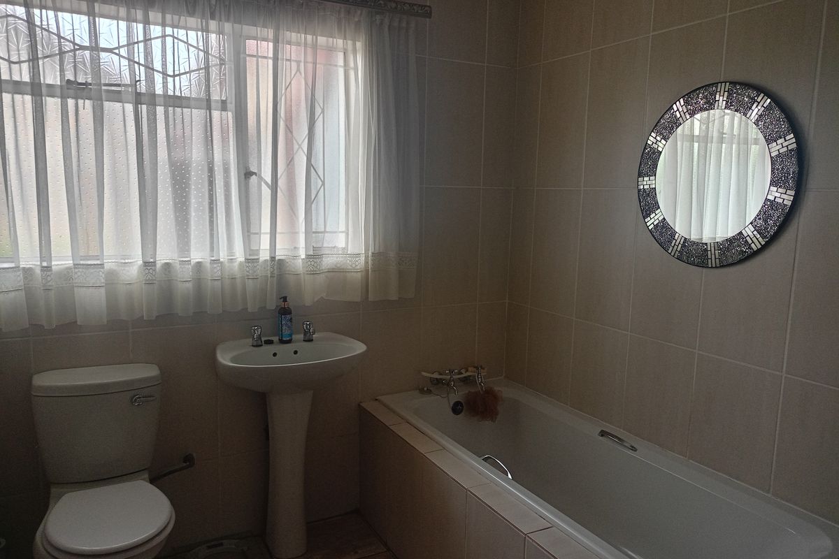 A functional bathroom featuring a pedestal basin, a built-in bathtub, and neutral wall tiling, providing a clean and practical space.