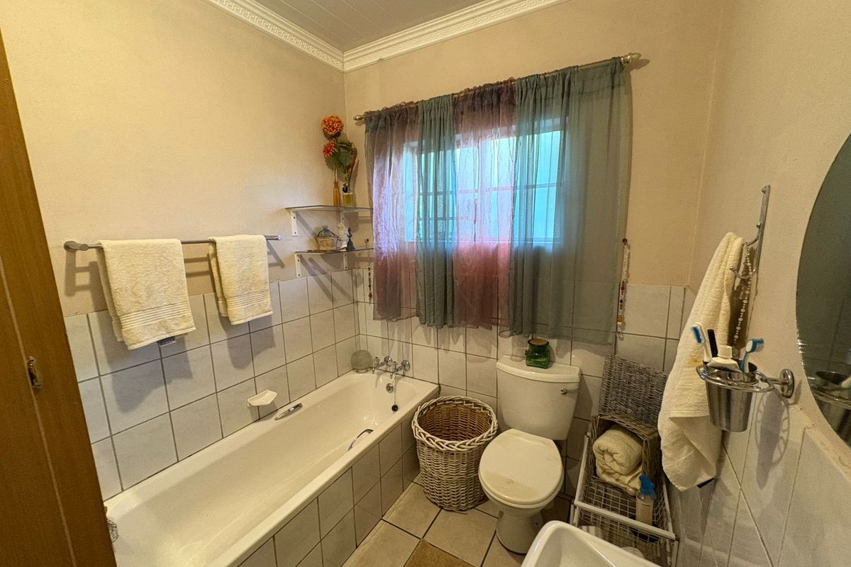 A functional bathroom featuring a built-in bathtub, ceramic tiling, and standard sanitary fixtures, offering a practical layout with potential for cosmetic updates.