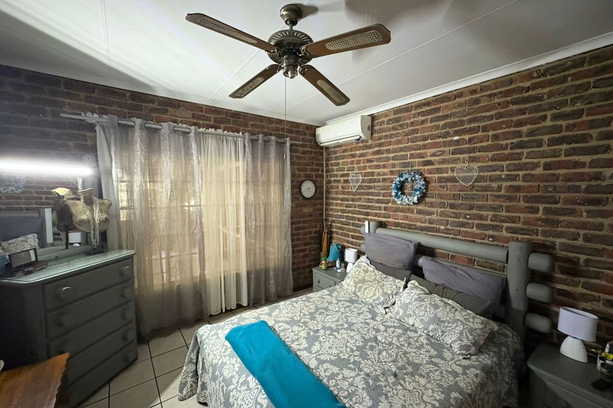A bedroom featuring exposed brick walls, a ceiling fan, and a wall-mounted air conditioning unit, providing a rustic aesthetic with functional climate control.