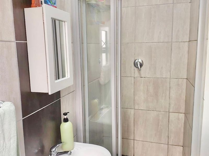 A functional bathroom featuring a shower enclosure with tiled walls and a pedestal basin with a wall-mounted medicine cabinet.