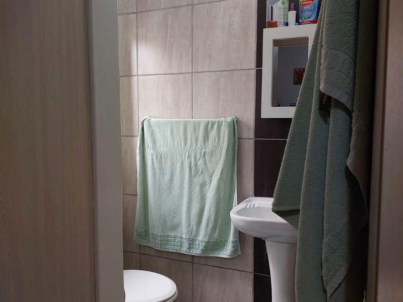 A compact bathroom featuring a pedestal sink, toilet, and neutral-toned wall and floor tiling.