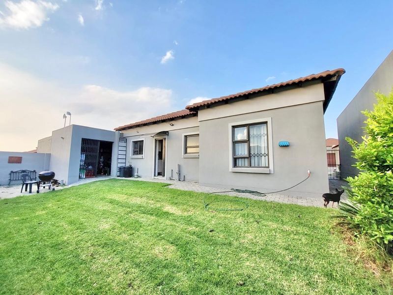 Rear view of the townhouse featuring a well-maintained lawn, paved patio area, and secure exterior access points.
