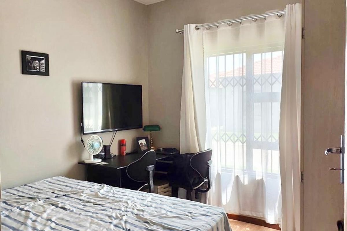 A functional bedroom featuring laminate flooring, coving, and a window fitted with a security gate.