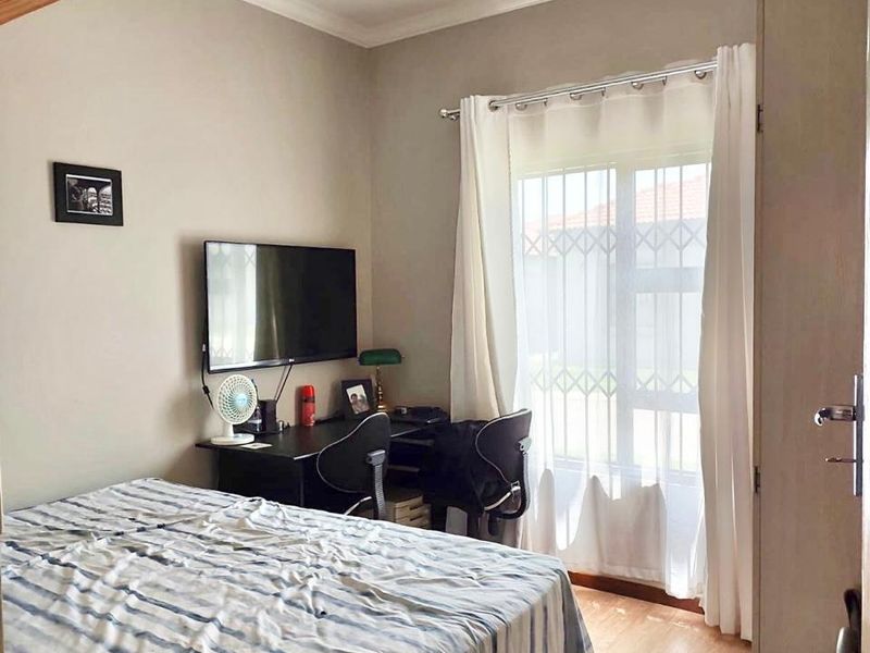 A functional bedroom featuring laminate flooring, coving, and a window fitted with a security gate.