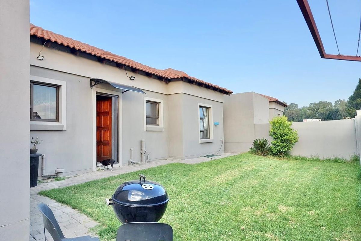 Rear view of the townhouse featuring a private garden, paved walkway, and terracotta tiled roof.