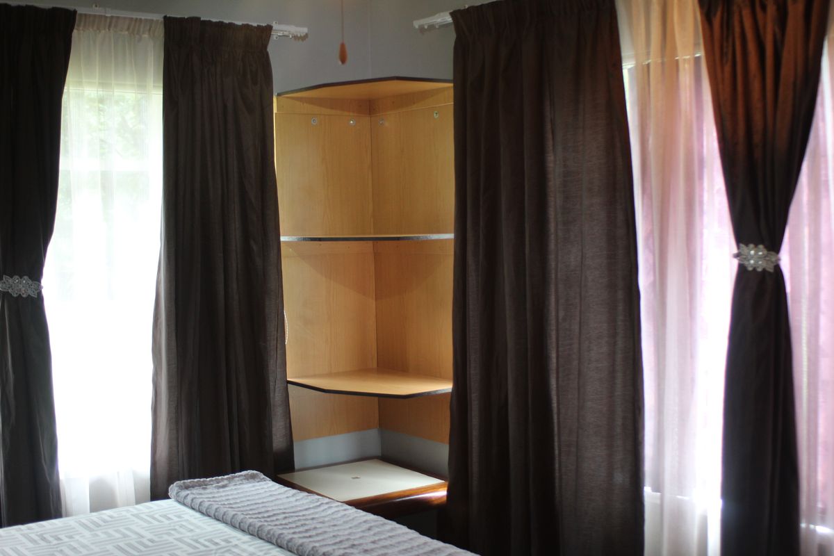 A bedroom featuring built-in corner shelving units positioned between two windows with curtains.