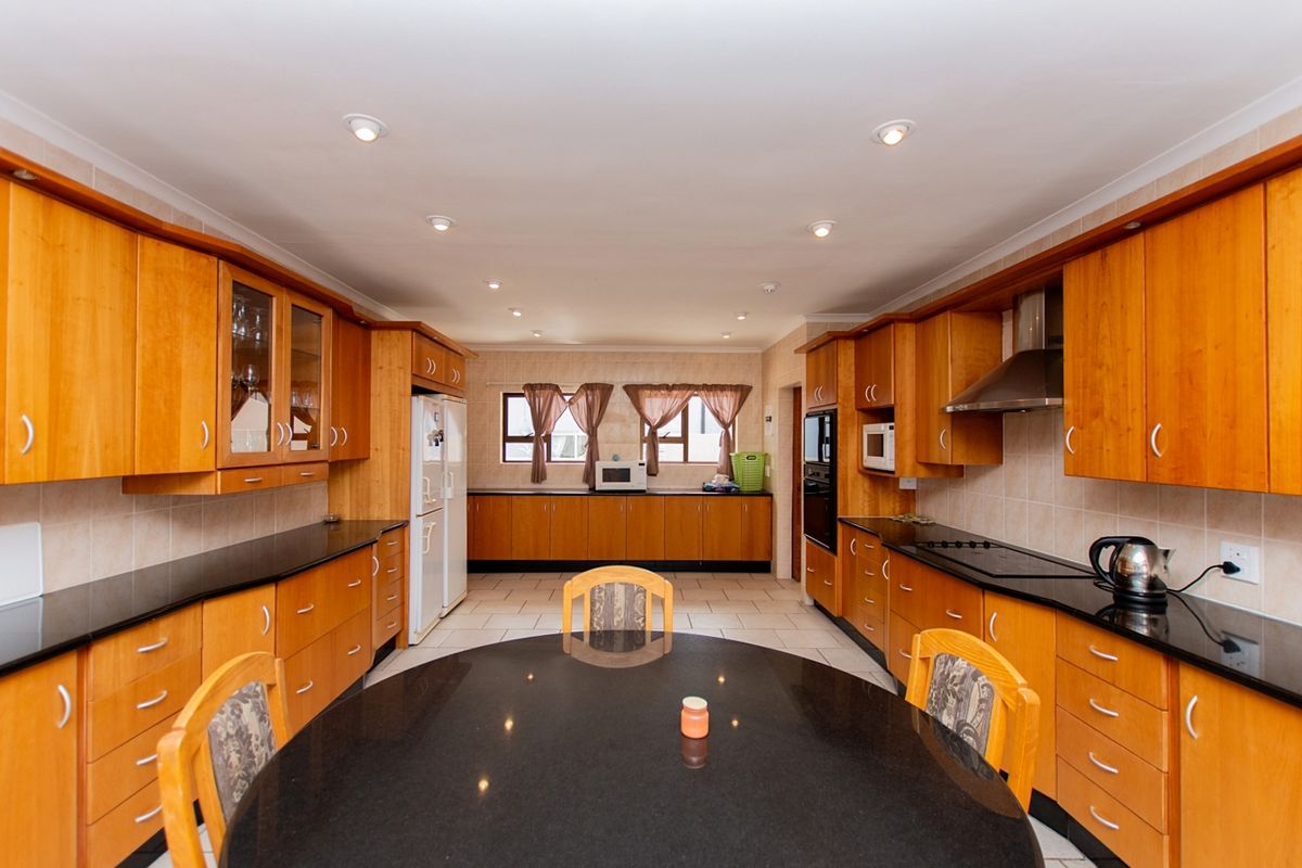 Spacious kitchen featuring extensive wooden cabinetry, black granite countertops, built-in oven, extractor fan, and tiled flooring with a central dining area.