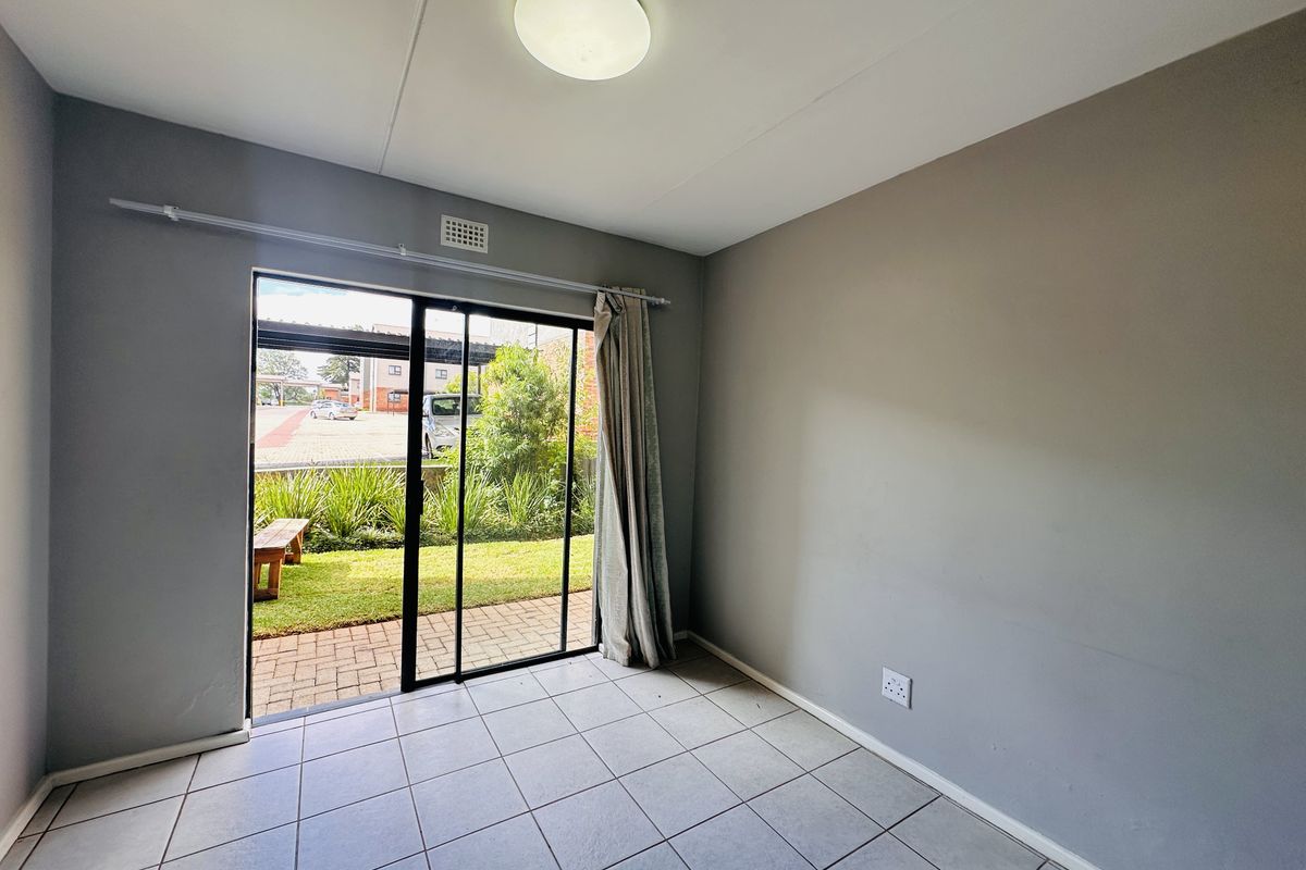 An empty living room featuring neutral grey walls, ceramic tiled flooring, and a sliding glass door providing direct access to an outdoor patio area.