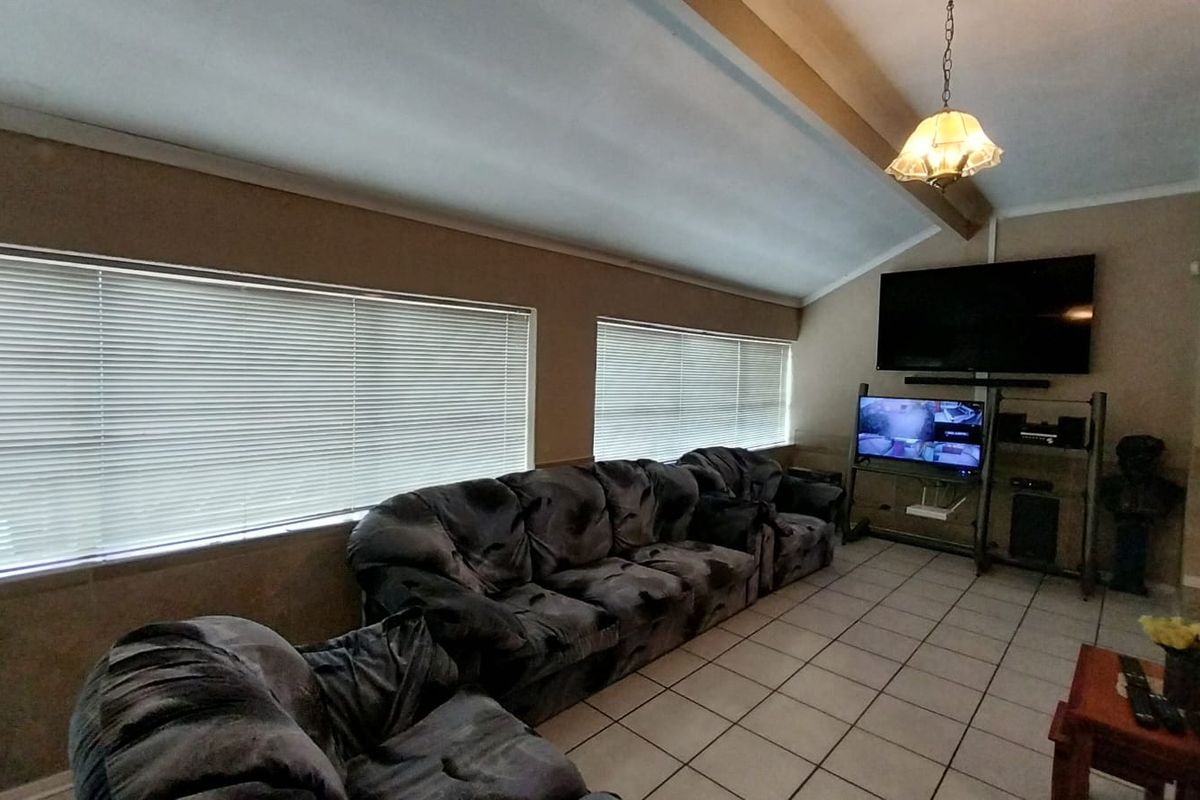 A living room featuring vaulted ceilings, tiled flooring, and large windows with fitted blinds, providing a functional and comfortable space.