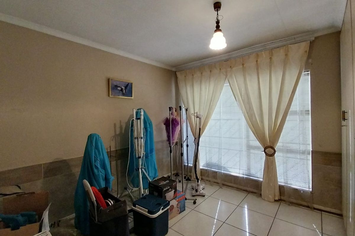 A bedroom featuring tiled flooring, built-in cupboards, and a large window with fitted blinds and curtains.