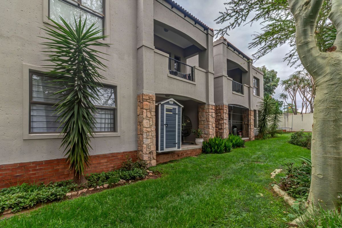Rear view of the apartment building featuring stone and brick detailing, private balconies with metal railings, and a well-maintained garden area.