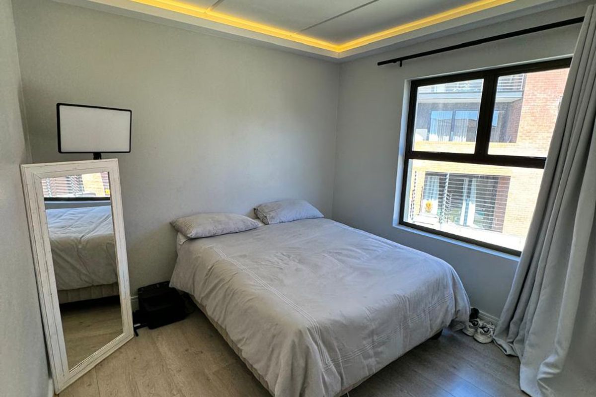 A well-maintained bedroom featuring modern recessed ceiling lighting, light-toned laminate flooring, and a large window providing natural light.