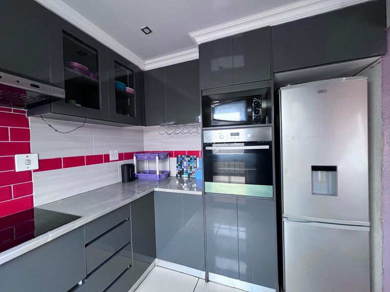 Modern kitchen featuring dark grey high-gloss cabinetry, integrated appliances including an oven and microwave, and a contrasting tiled backsplash.