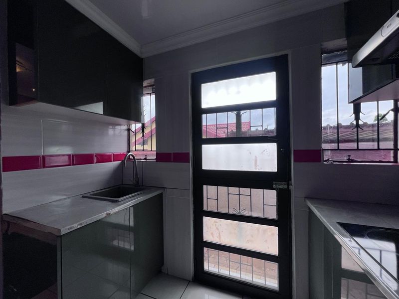 A compact scullery area featuring built-in cabinetry, a stainless steel sink, and a security door leading to the exterior.