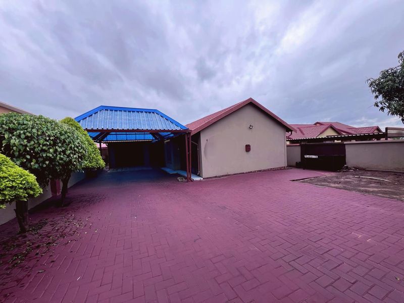 Front exterior view of the property featuring a large paved driveway, a covered carport, and perimeter boundary walls.