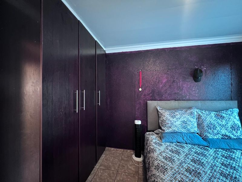 Bedroom featuring dark built-in cupboards, tiled flooring, and a textured purple feature wall.