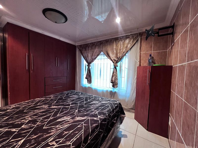 A bedroom featuring built-in cupboards, tiled walls, and tiled flooring, with security bars on the window.