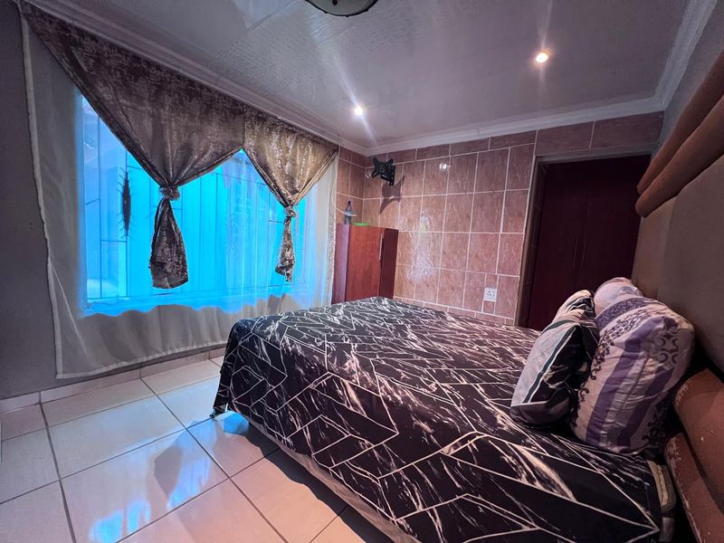 A bedroom featuring tiled flooring, a tiled accent wall, recessed lighting, and built-in storage, with security bars on the window.